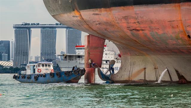 Nicht nur Segelschiffe brauchen Wartung. Ein grosser Öltanker wird an der Schraube repariert. Im Hintergrund der Komplex der "Mariana Bay Sands", gesehen in Singapur.
